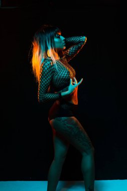 Bangs ve renkli saç ile alternatif model bir fishnet üst giyen teal ve turuncu ışık altında pozlar