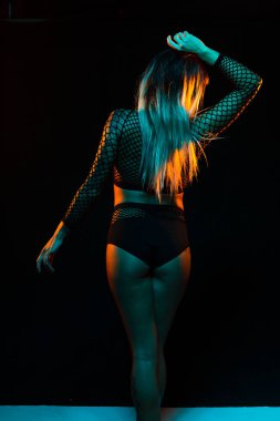 Bangs ve renkli saç ile alternatif model bir fishnet üst giyen teal ve turuncu ışık altında pozlar