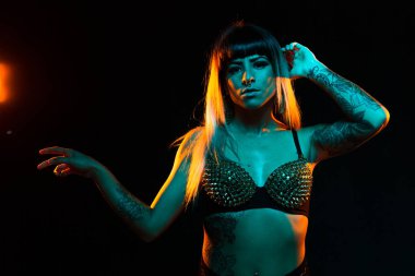 Bangs ve renkli saç ile alternatif model bir fishnet üst giyen teal ve turuncu ışık altında pozlar