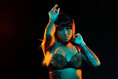 Bangs ve renkli saç ile alternatif model bir fishnet üst giyen teal ve turuncu ışık altında pozlar