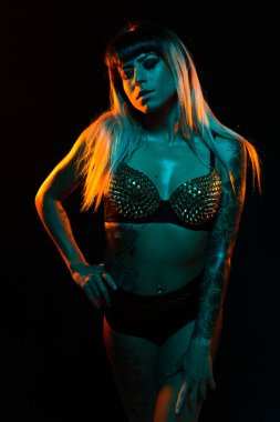 Bangs ve renkli saç ile alternatif model bir fishnet üst giyen teal ve turuncu ışık altında pozlar