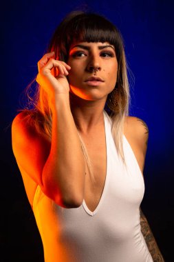 Patlama ve renkli saç ile alternatif model beyaz bir mayo giyen mavi ve turuncu ışık altında pozlar