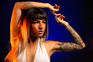 Patlama ve renkli saç ile alternatif model beyaz bir mayo giyen mavi ve turuncu ışık altında pozlar