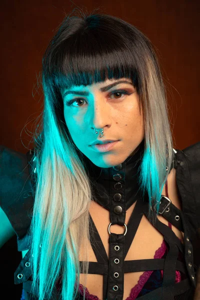 Alternative model with bangs and colored hair poses under blue light wearing a leather outfit