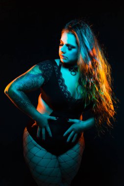 Renkli saç ve dantel bodysuit ve fileleri ile kıvrımlı alternatif model mavi ve turuncu aydınlatma altında pozlar