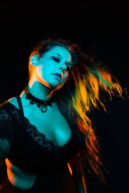 Renkli saç ve dantel bodysuit ve fileleri ile kıvrımlı alternatif model mavi ve turuncu aydınlatma altında pozlar