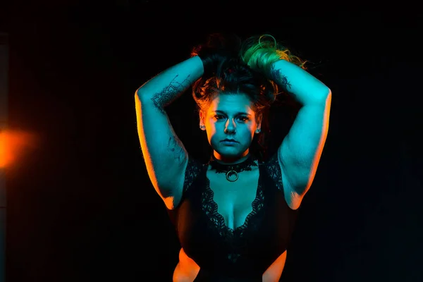 Close up portrait of curvy alternative model with colored hair and lace bodysuit and fishnets under blue and orange lighting