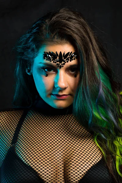 Close up portrait of curvy alternative model with colored hair and mesh clothing under blue lighting
