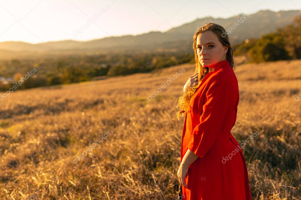 Tan mixed race woman wearing red dress stands alone in open field