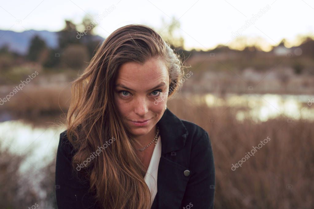 Tan mixed race woman wearing mens waistcoat poses by a winter pond