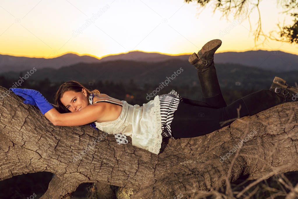 Tan mixed race woman lounges on a large oak tree branch wearing dress