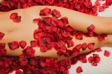 Beyaz kadının kalçaları, uylukları ve midesi yatakta gül yapraklarıyla kaplı