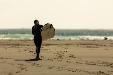 Surfers wearing wetsuits approach the green waters of Mendocino'