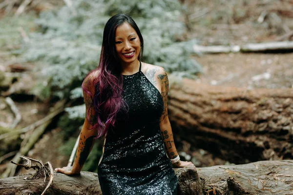 Asian tattooed woman in black evening dress poses on a fallen re — Stock Photo, Image