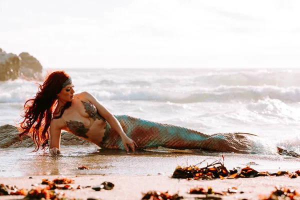Кавказская рыжая женщина с хвостом русалки лежит на пляже — стоковое фото