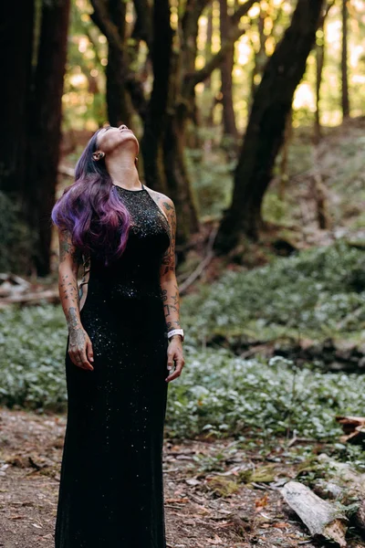 Азиатская татуированная женщина в черном вечернем платье стоит в лесу — стоковое фото