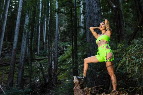 Asiática tatuada mujer en neón rave ropa poses en un redwood fo — Foto de Stock