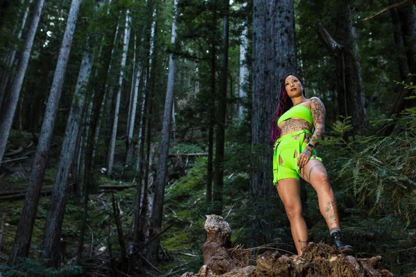 Asiática tatuada mujer en neón rave ropa poses en un redwood fo — Foto de Stock