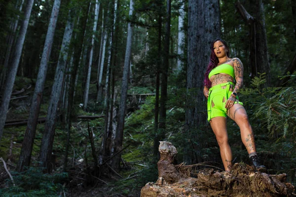 Asiática tatuada mujer en neón rave ropa poses en un redwood fo — Foto de Stock