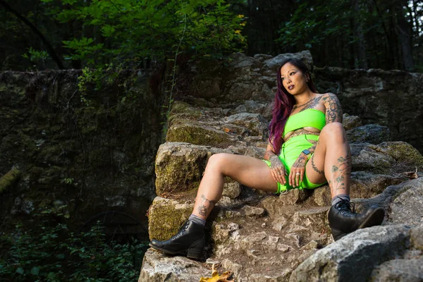 Asiática tatuada mujer en neón rave ropa poses en un abandonado — Foto de Stock