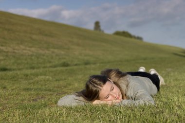 A girl is lying relaxed on the grass and has his eyes closed