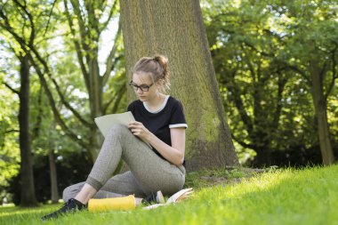 Bir ağacın altında oturan genç bir kadın ve bir klasörde yazıyor