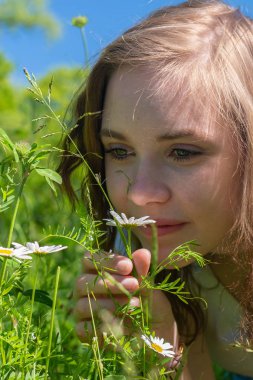 Bir kadın parkta çiçeklerin üzerinde kokuyor.