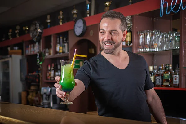 A smiling waiter serves a cocktail at a counter