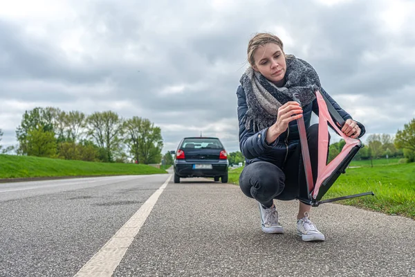 Женщина с поломкой машины строит свой предупреждающий треугольник — стоковое фото