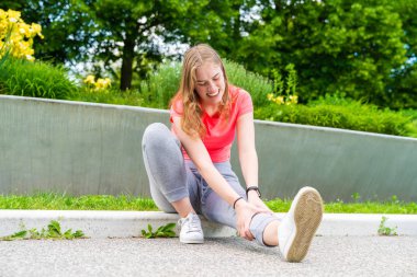 Bir kadın yerde oturuyor, yaralı bacağını tutuyor.