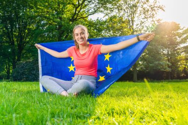 young woman is holding a European flag behind her and is smiling