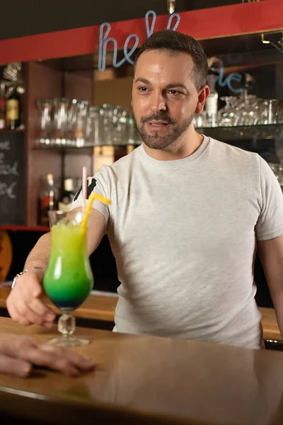 Smiling waiter serves a green cocktail at a counter