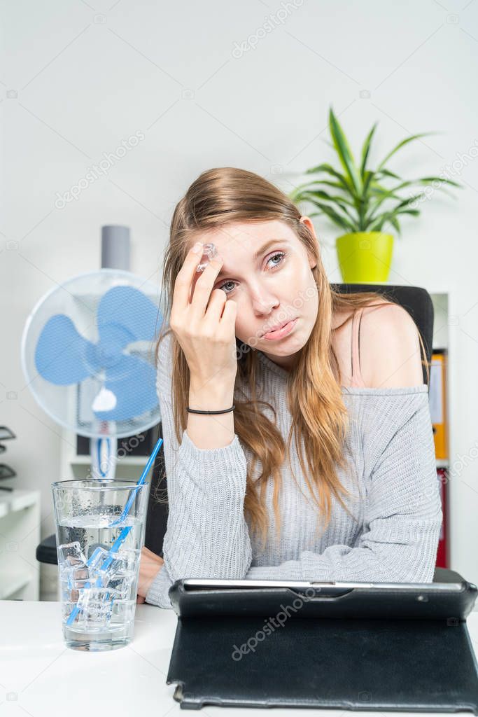 young woman in the office cools her forehead with an ice cube