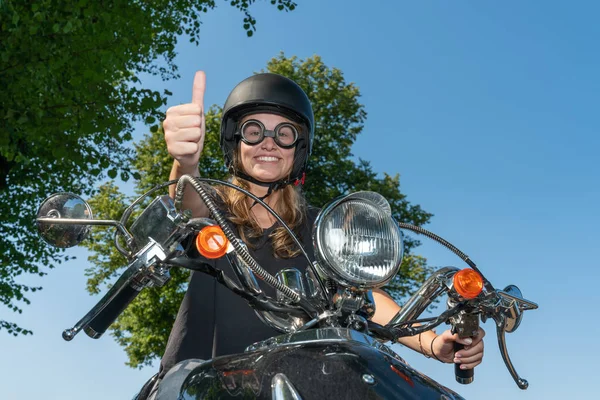 A young woman drives a scooter and holds her thumb up