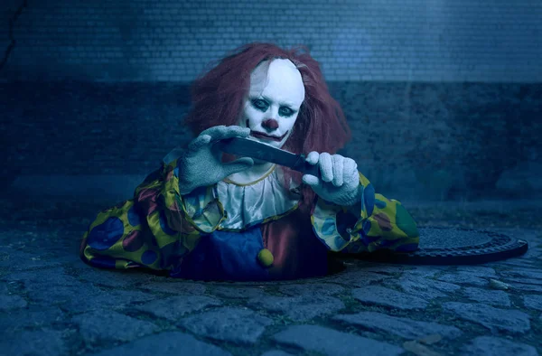 Een killer clown met een mes dat uit het riool stijgt — Stockfoto