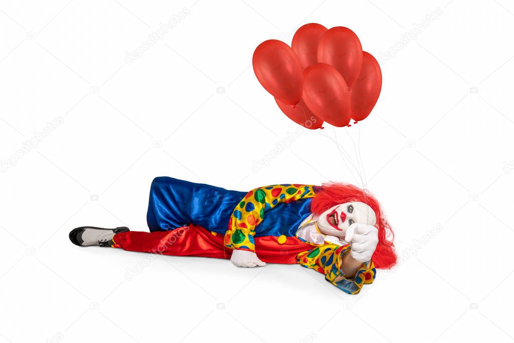A cheerful clown lies on the floor holding balloons in his hand