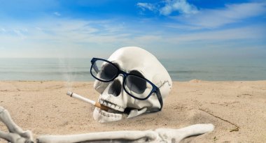 Sigara bağımlılığı hakkında bir kavram. Sigaralı bir iskelet kumda yatıyor.