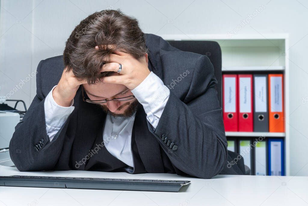 An over-worked businessman in the office holds his head