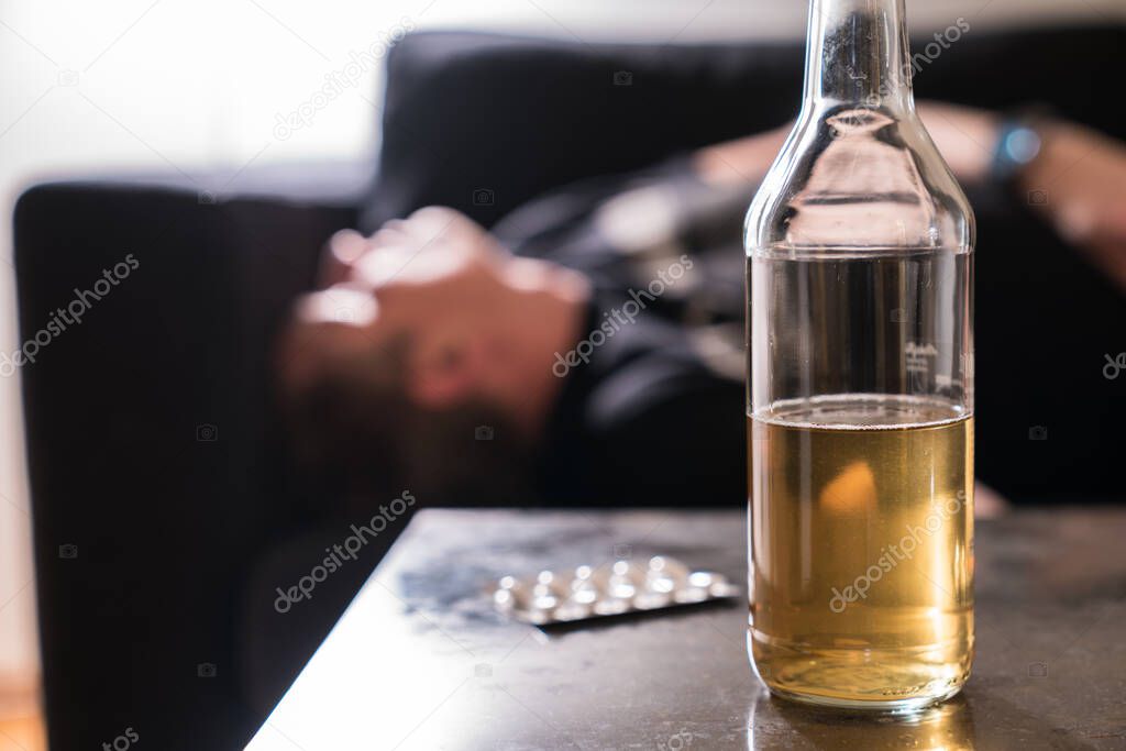Drunk man with alcohol bottle and pills on the table sleeping on couch