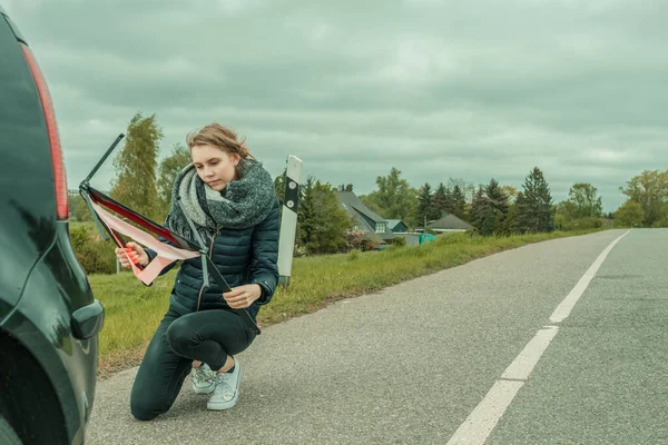 Молодая женщина с поломкой машины пытается собрать предупреждающий треугольник — стоковое фото
