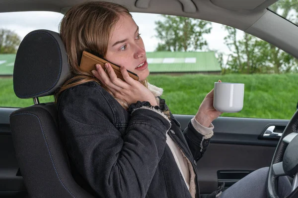 한 여자 가차를 운전하면서 전화로 커피를 마시고 있다 — 스톡 사진