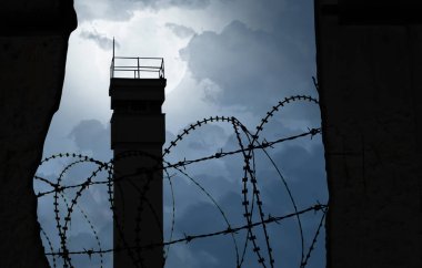 Bölüm sembolü olarak dikenli telleri olan bir duvarın arkasındaki gözetleme kulesi.