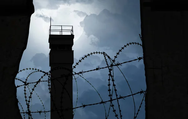 Bölüm sembolü olarak dikenli telleri olan bir duvarın arkasındaki gözetleme kulesi.
