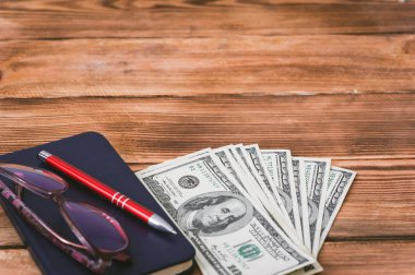 Dolar, defter, gözlük ve ahşap zemin üzerine kalem. İş kavramı