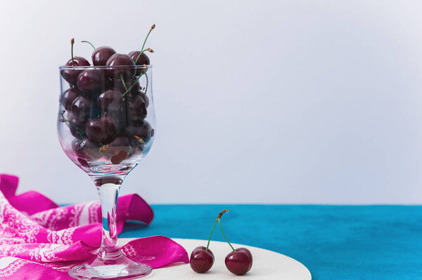 Cherries in glass on a blue and wooden background with a copy space for text. Top view, healthy food.