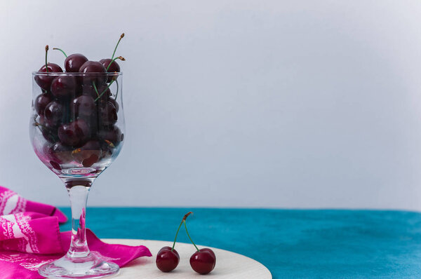 Cherries in glass on a blue and wooden background with a copy space for text. Top view, healthy food. 