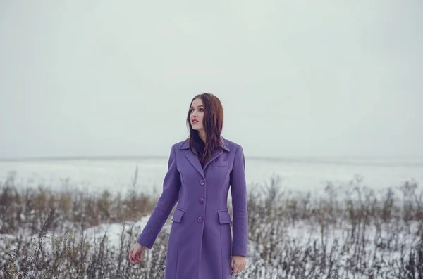 Beautiful smiling woman in violet coat walking outside in the winter time. Copy space for text