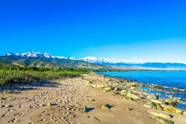 Tian Shan dağ silsilesi Issyk Kul göl kıyısı taş taş Sandy Beach kar ile şapkalı