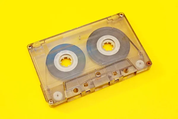 Old transparent audio cassette located on a yellow background
