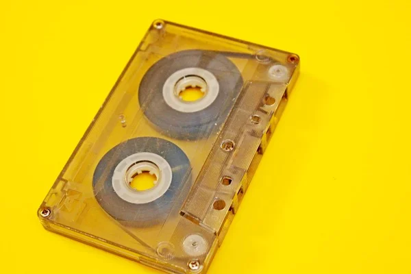 Old transparent audio cassette located on a yellow background